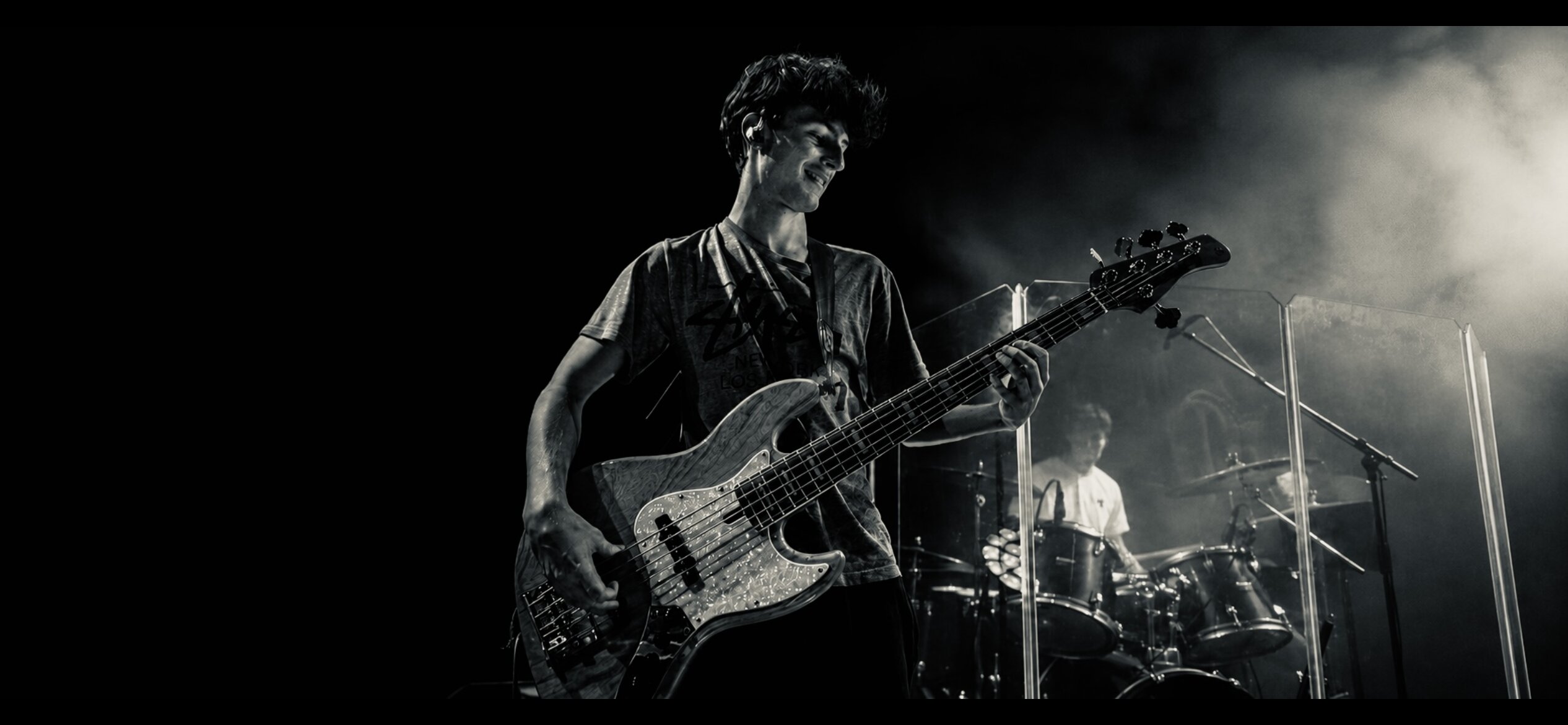Charlie Neale playing bass live on stage, with a drummer behind him